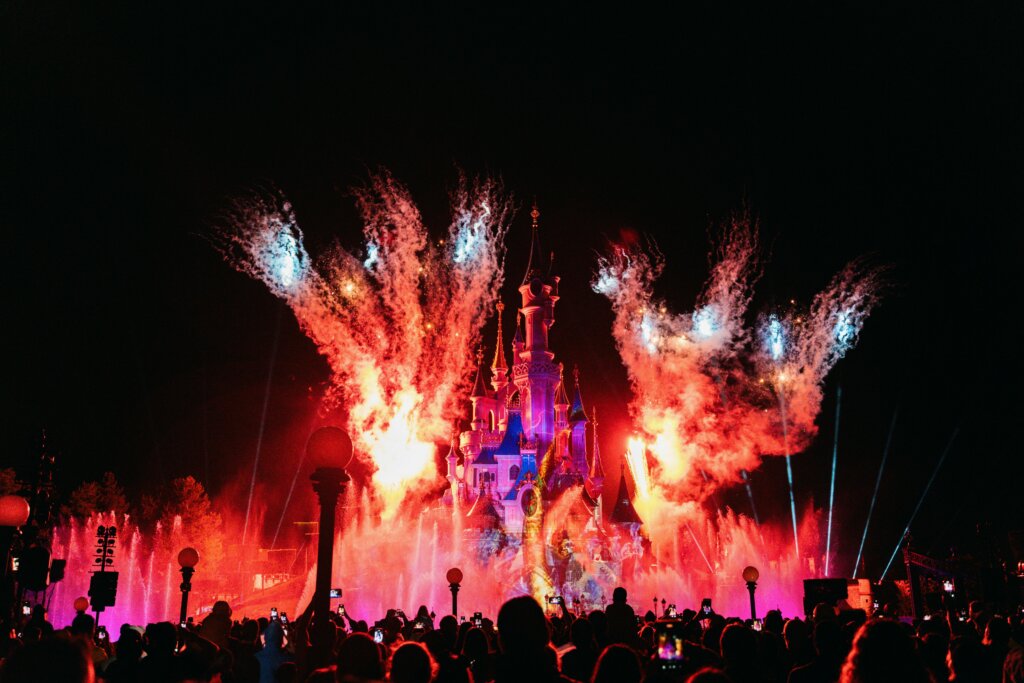 Fireworks burst over Cinderella Castle during nighttime show at Disney theme park with crowd watching.