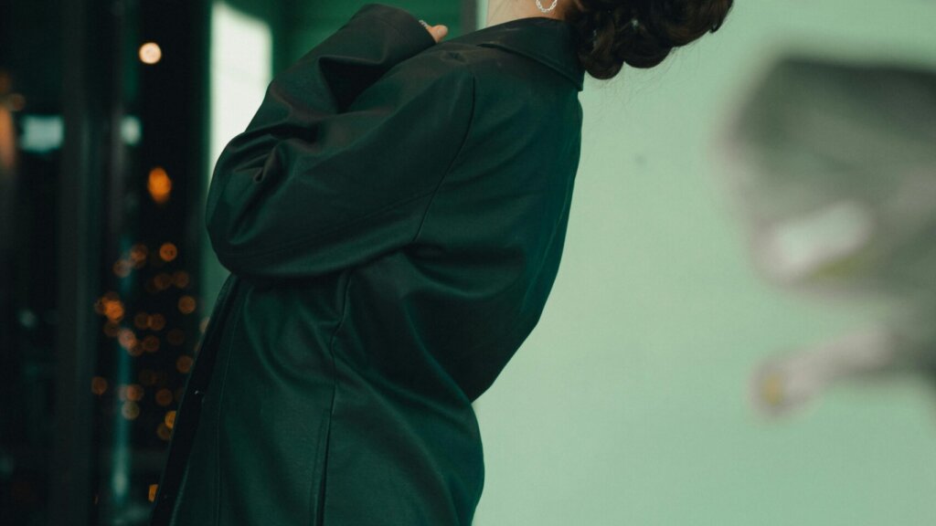 A person in a dark green coat leaning back against a green background.