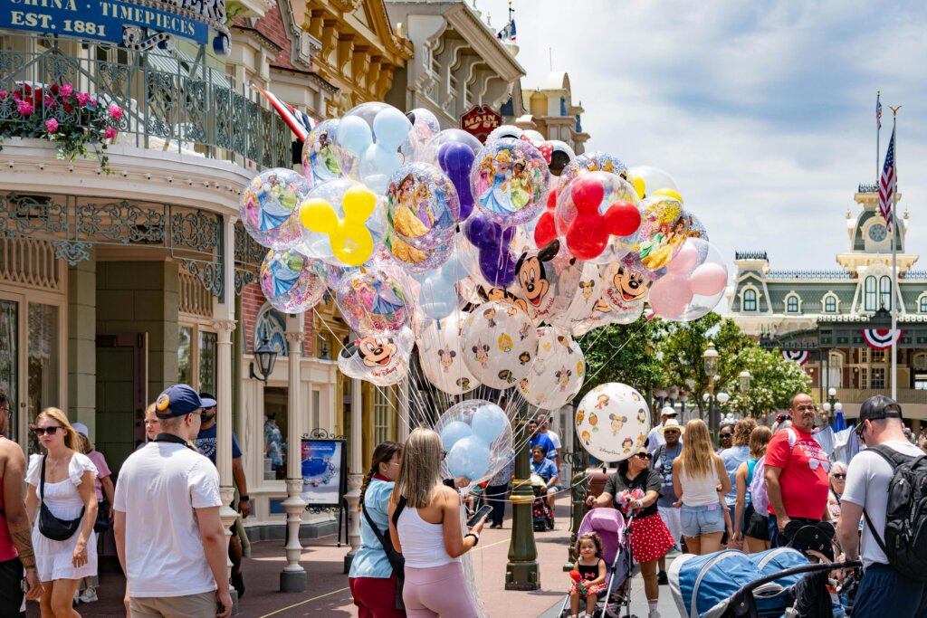 Visitors walking along Main Street holding Disney character balloons in a busy theme park.