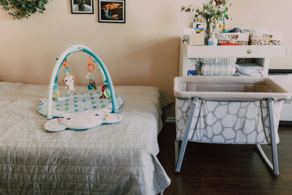 Nursery setup with baby bassinet, changing table, diapers, and toys arranged in a bedroom.