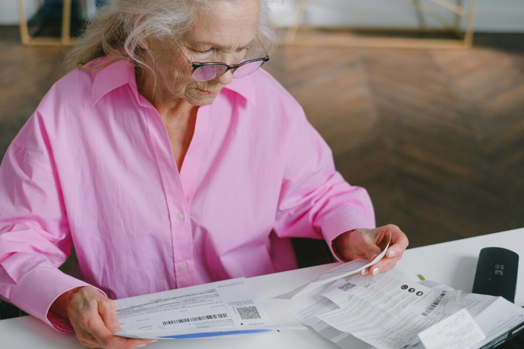 Older woman reviewing bills and documents at a table, focusing on paperwork.