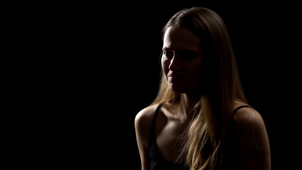 Silhouetted portrait of a woman with long hair against a dark background. Dramatic lighting highlights her hair and profile.