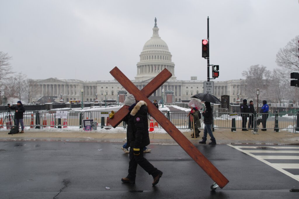 Person carrying a large wooden cross past the U.S. Capitol building in Washington, D.C.
