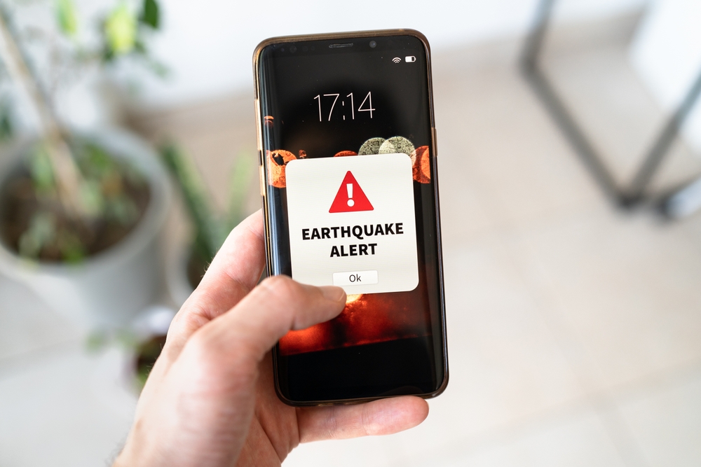 Hand holding smartphone displaying earthquake alert notification on screen.