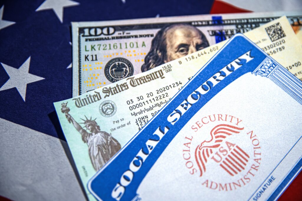 Social Security card with U.S. Treasury check and $100 bill on American flag background.