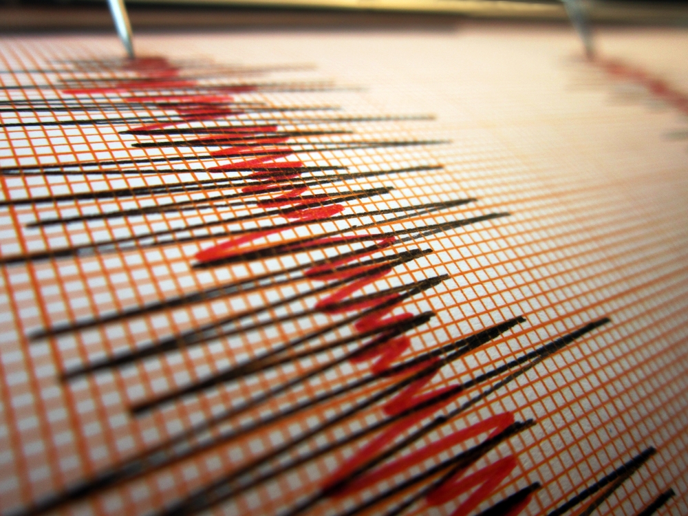Seismograph recording earthquake activity with red waveform lines on graph paper.