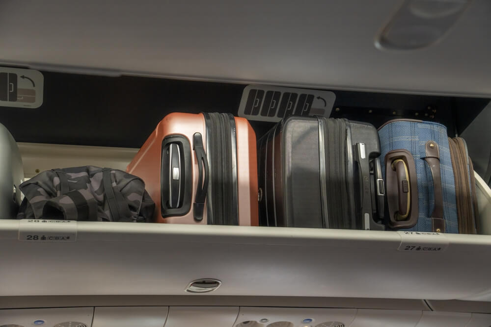 Carry-on suitcases stored in overhead bin inside airplane cabin.