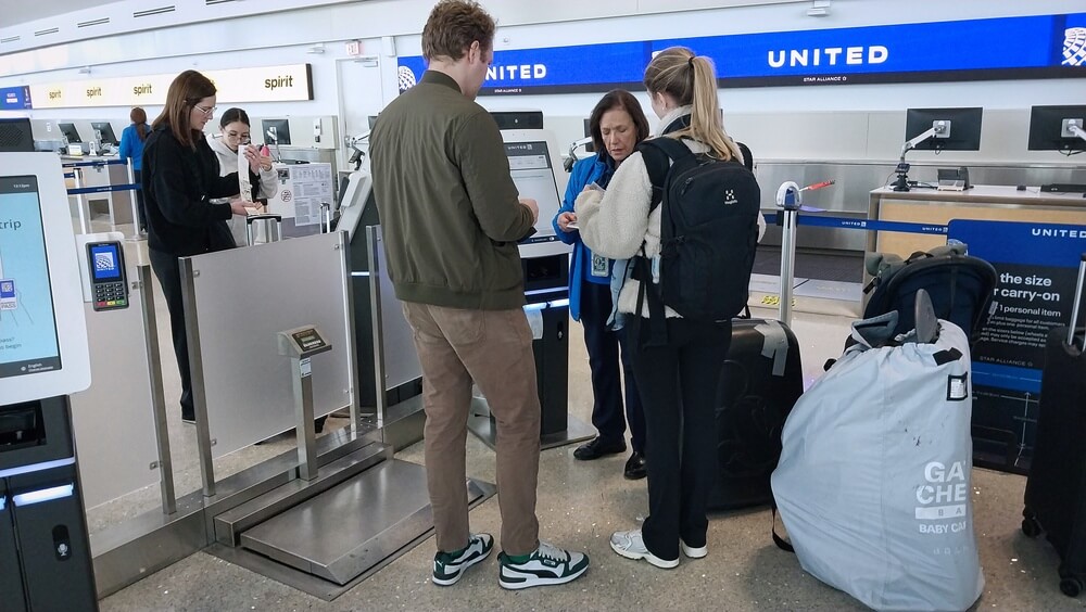 Passengers using self-service kiosk at United Airlines check-in counter with agent assistance.