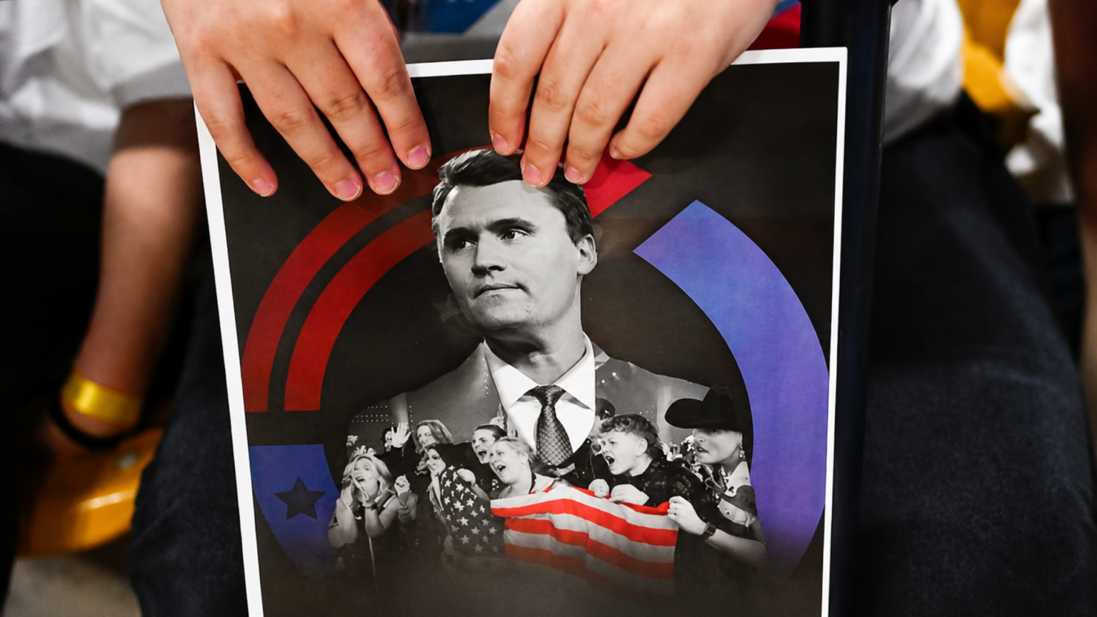 Tennessee County Pays $835,000 To Resolve First Amendment Suit After Jailing Man Over Political Meme A close-up shot of hands holding a political flyer featuring a portrait of conservative activist Charlie Kirk surrounded by supporters and an American flag.