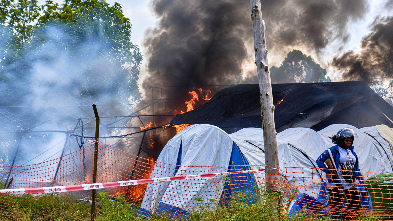 Rising Anger Over Ebola Outbreak Leads Residents to Burn Treatment Center in Congo Fire burning behind tents as smoke rises over a fenced area.