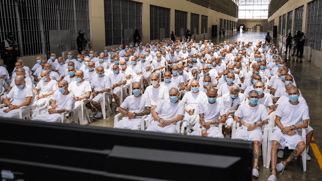 Masked inmates seated inside a prison cell block during a gathering at a correctional facility.