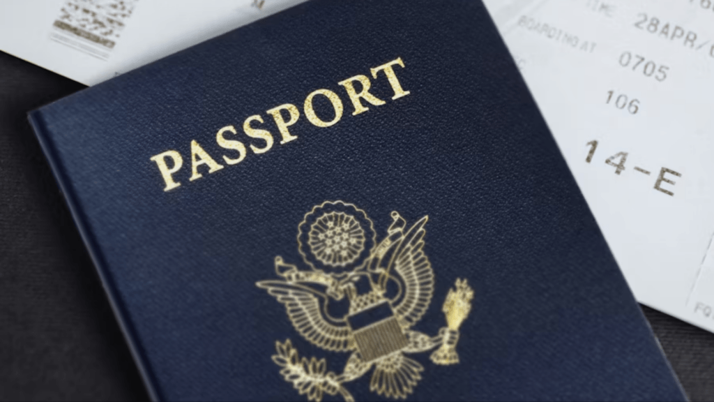 A close-up of a navy blue U.S. Passport with gold lettering, partially resting on a printed boarding pass.