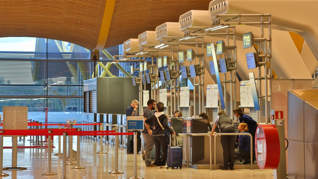 Passengers standing at check-in counters inside a spacious, modern airport terminal.