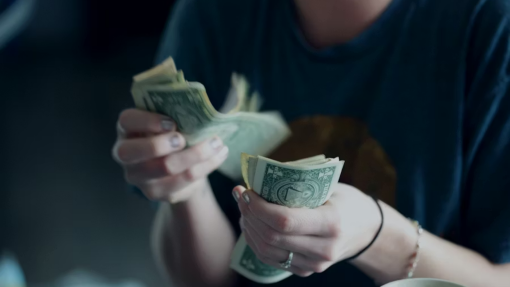 A shallow-focus close-up shot of a person's hands rapidly counting through a thick stack of green one-dollar bills, capturing the daily consumer struggle with purchasing power, cash budgeting, and inflation.