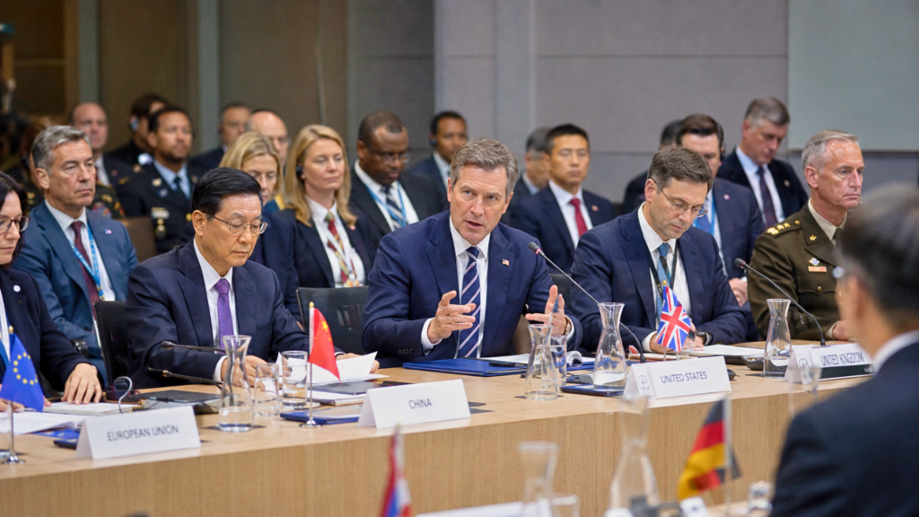 International delegates, including representatives seated behind country nameplates for China, the United States, and the United Kingdom, participate in a formal panel discussion.