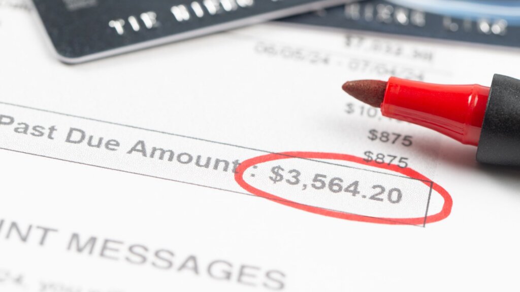 Close up of a credit card bill showing “Past Due Amount” with “$3,564.20” circled in red beside a red marker pen resting on the paper.