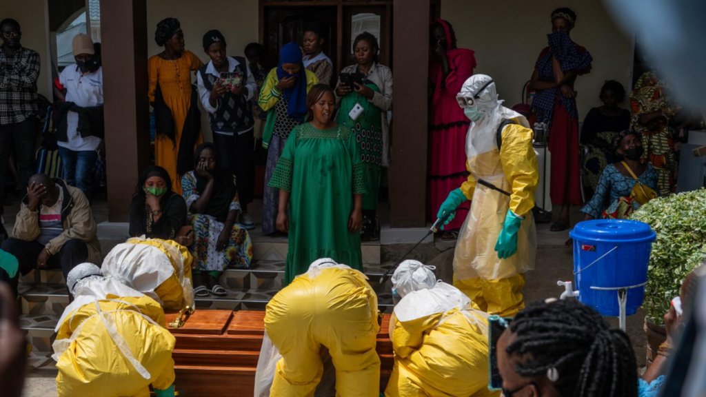 Workers in protective suits handling a coffin during a funeral.