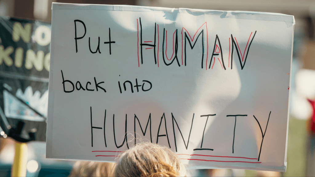 Protest sign reading “Put Human back into Humanity” held at a public demonstration.