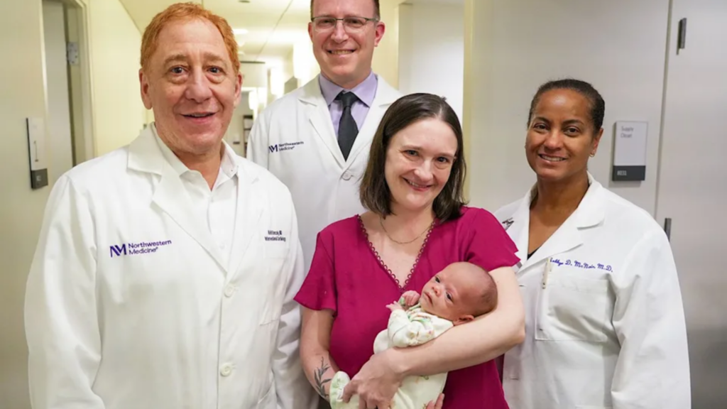 A celebratory group shot in a hospital hallway featuring three doctors in white Northwestern Medicine lab coats standing with a mother in a maroon top who is holding her newborn baby; they are all smiling at the camera, marking a successful discharge.