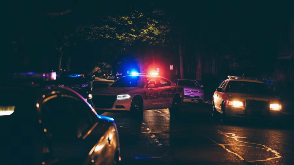 Police vehicles with flashing lights blocking a street at night during an emergency response.