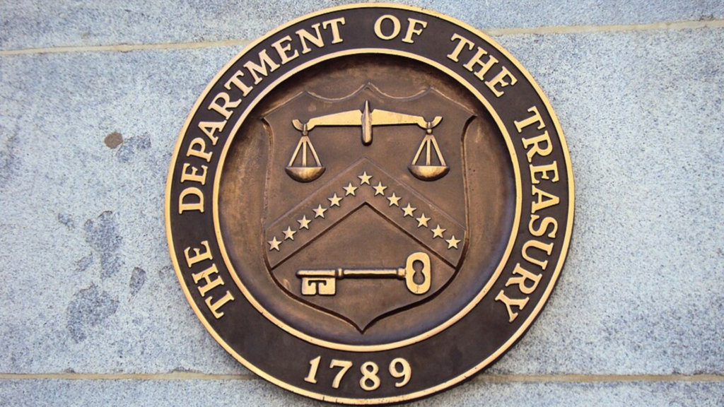 A bronze circular seal for the Department of the Treasury mounted on a grey stone wall.