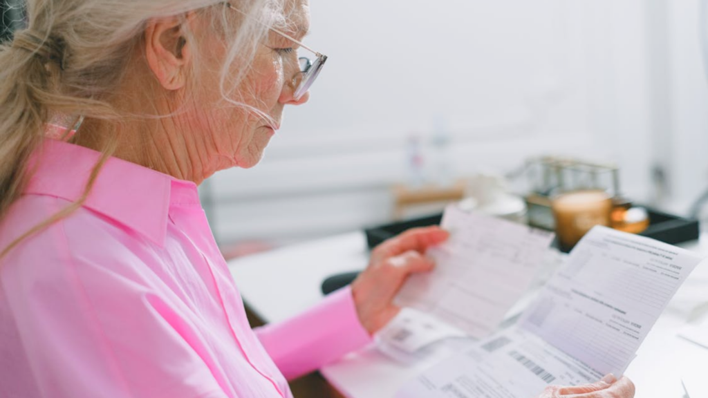 An older woman wearing glasses carefully reading medical bills and documents.