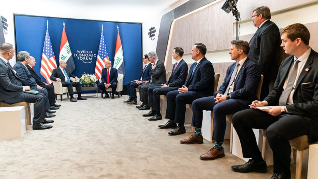 Donald Trump and another leader sit between the US and Iraq flags during a meeting at the World Economic Forum.