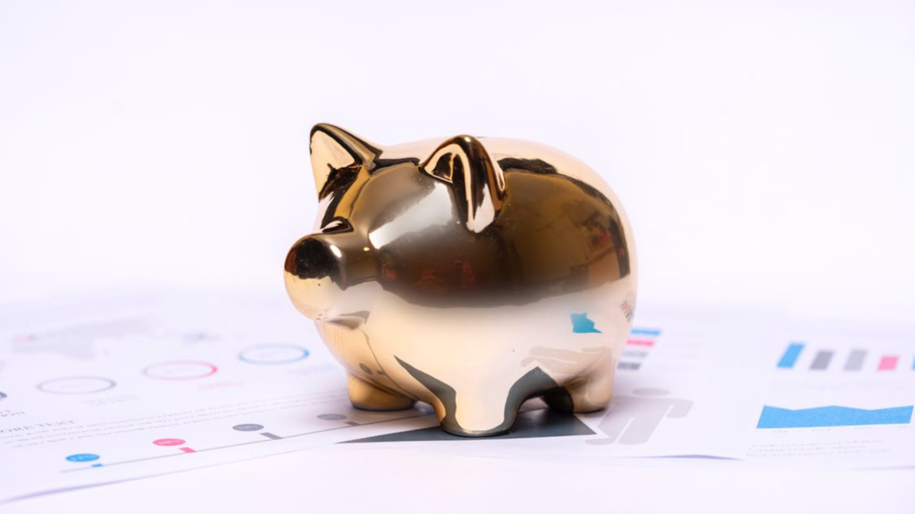 A shiny gold piggy bank rests on top of papers showing colorful financial charts and graphs.