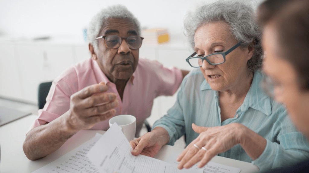 An older couple sits at a table looking over paperwork together during a meeting.