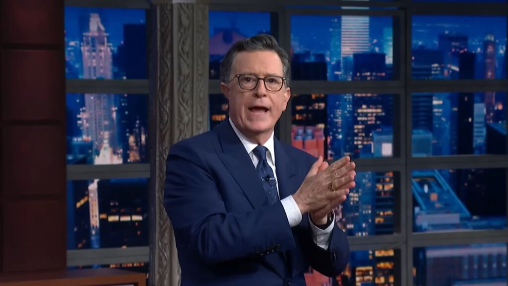 Stephen Colbert speaks onstage during the last episode of The Late Show, standing in front of the show’s nighttime cityscape backdrop.