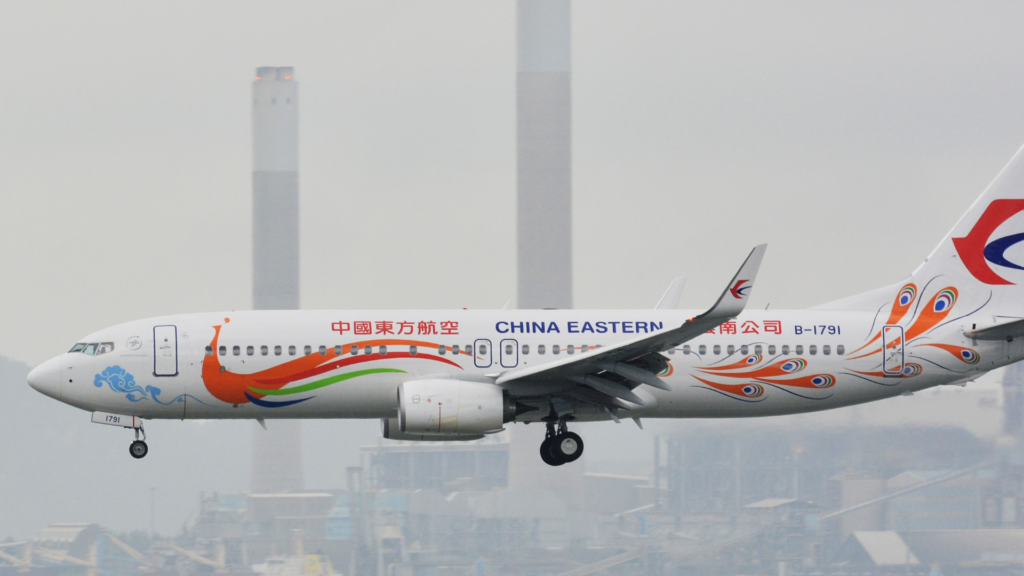 China Eastern Airlines Boeing 737 airplane, featuring a colorful orange and green peacock livery on its fuselage, is captured mid-flight with its landing gear deployed.