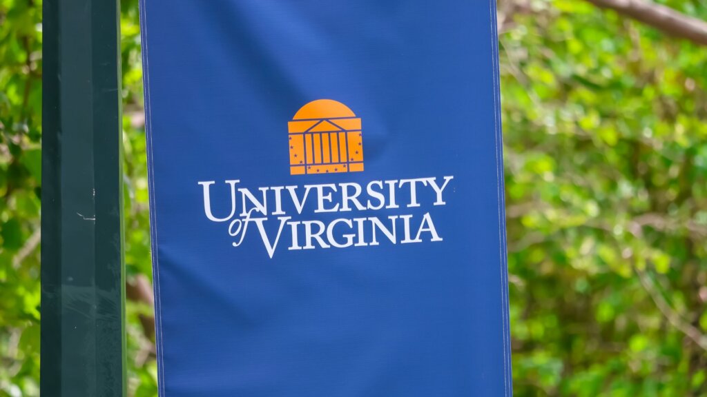 University of Virginia banner on campus pole with green trees in the background.