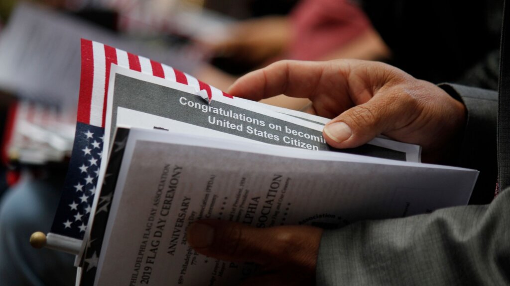 Person holding a congratulations pamphlet and small American flag at a citizenship ceremony.