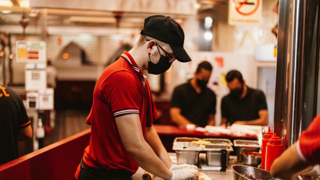 Fast food worker in uniform preparing food behind a restaurant counter.