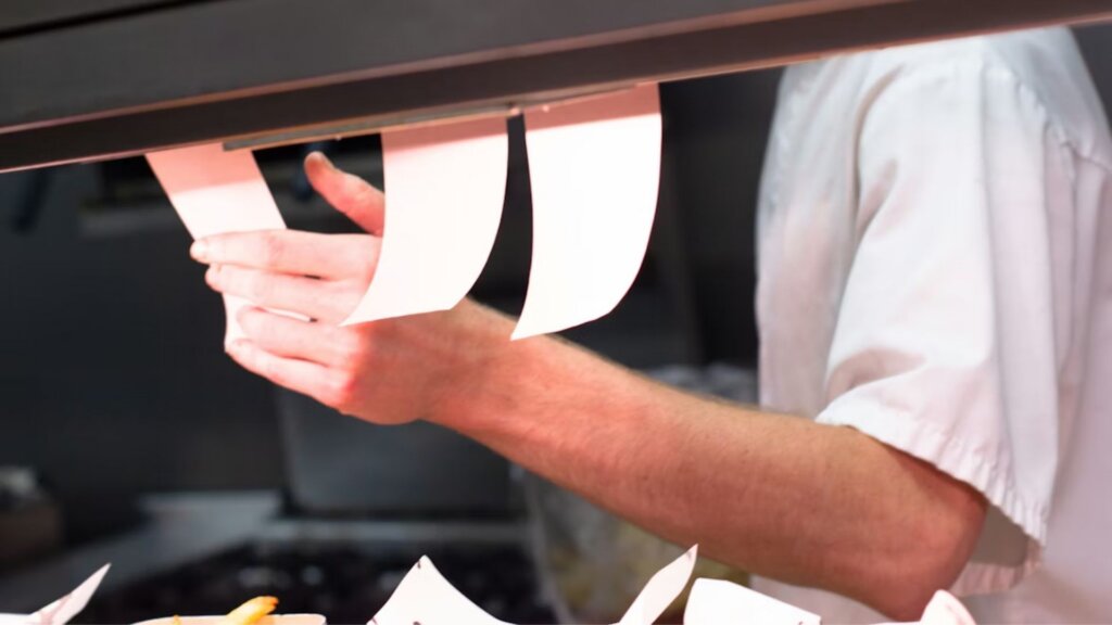 Kitchen worker pulling order tickets in a busy restaurant.
