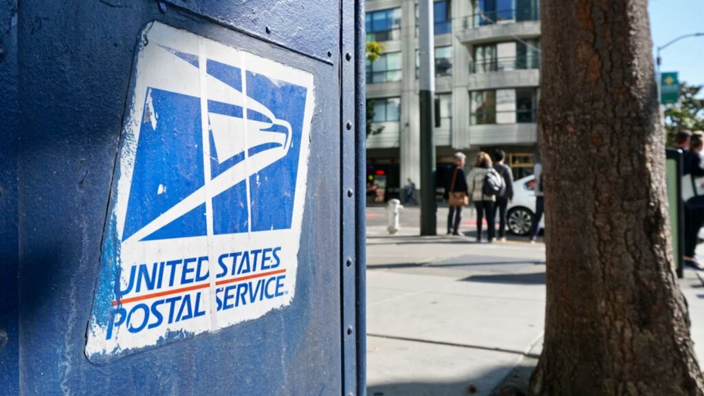 Close-up of a weathered United States Postal Service logo on a blue metal mailbox on a city street.