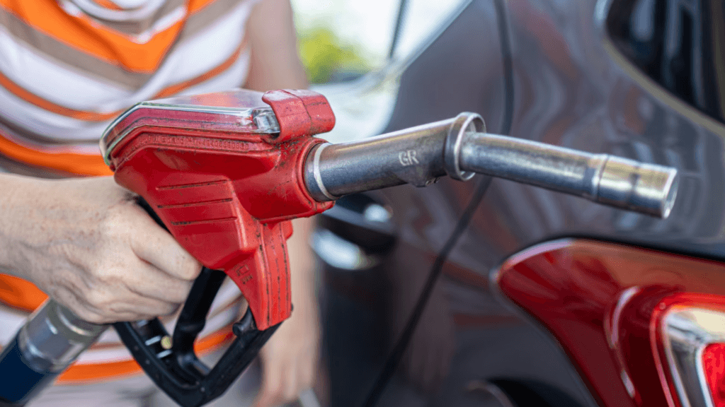 A close-up of a person's hand holding a red fuel nozzle while refueling a vehicle.