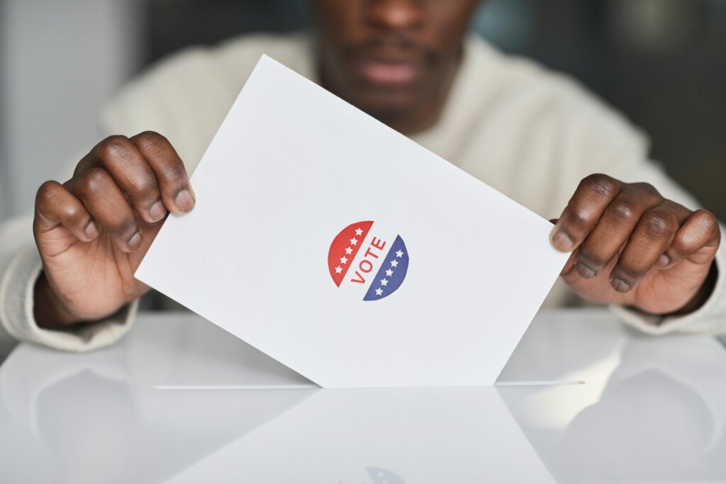 Voter placing a ballot with a “Vote” sticker into a ballot box during an election.