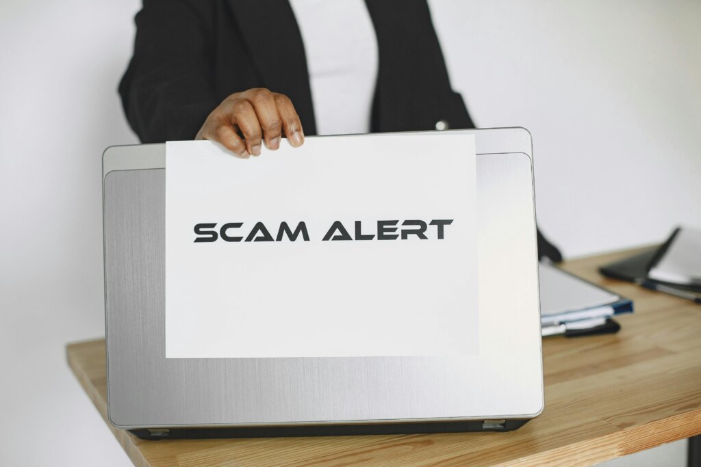 A person holding a “Scam Alert” sign in front of a laptop, symbolizing growing awareness about online fraud and cybercrime threats.