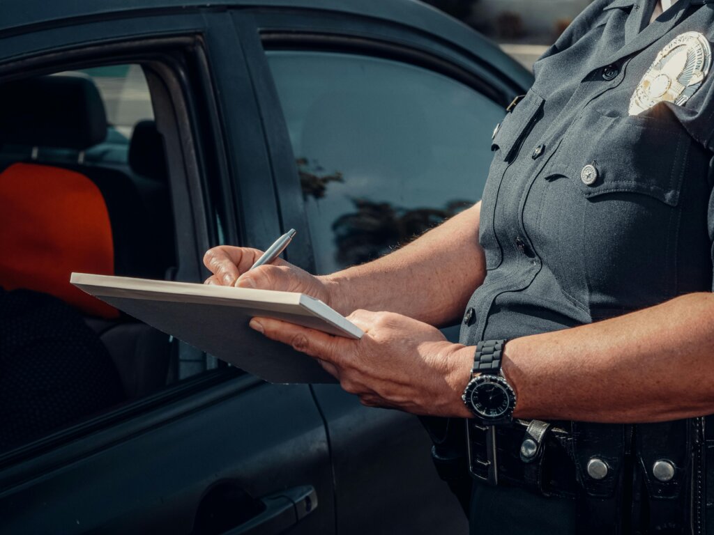 Police officer writing a citation beside a parked vehicle.