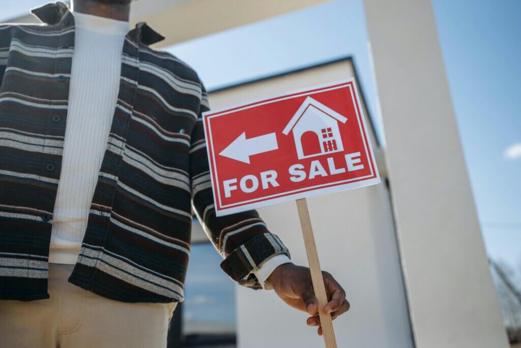 Person holding a “For Sale” sign outside a residential property.