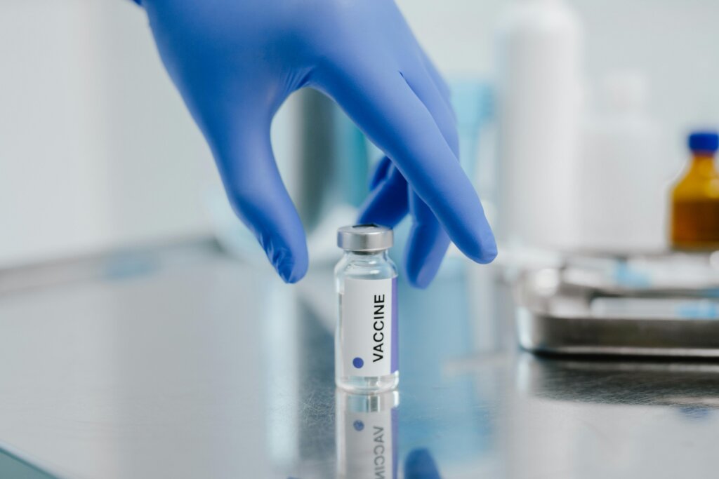 Gloved hand holding a vaccine vial in a medical setting.