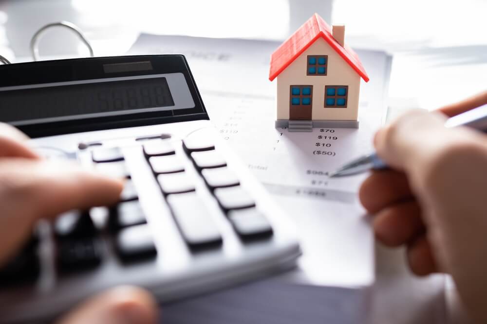 Calculator, paperwork, and model house illustrating home financing and mortgage costs.