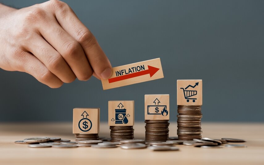 Hand placing an inflation block above stacked coins representing rising consumer costs.