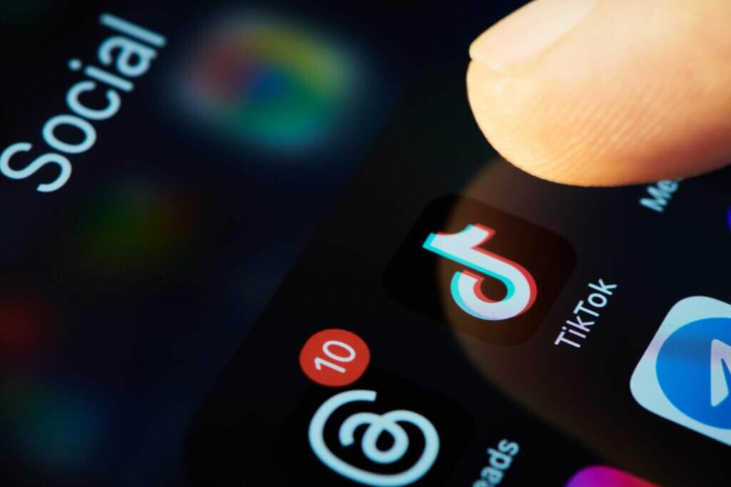 Finger hovering over the TikTok app icon on a smartphone screen.