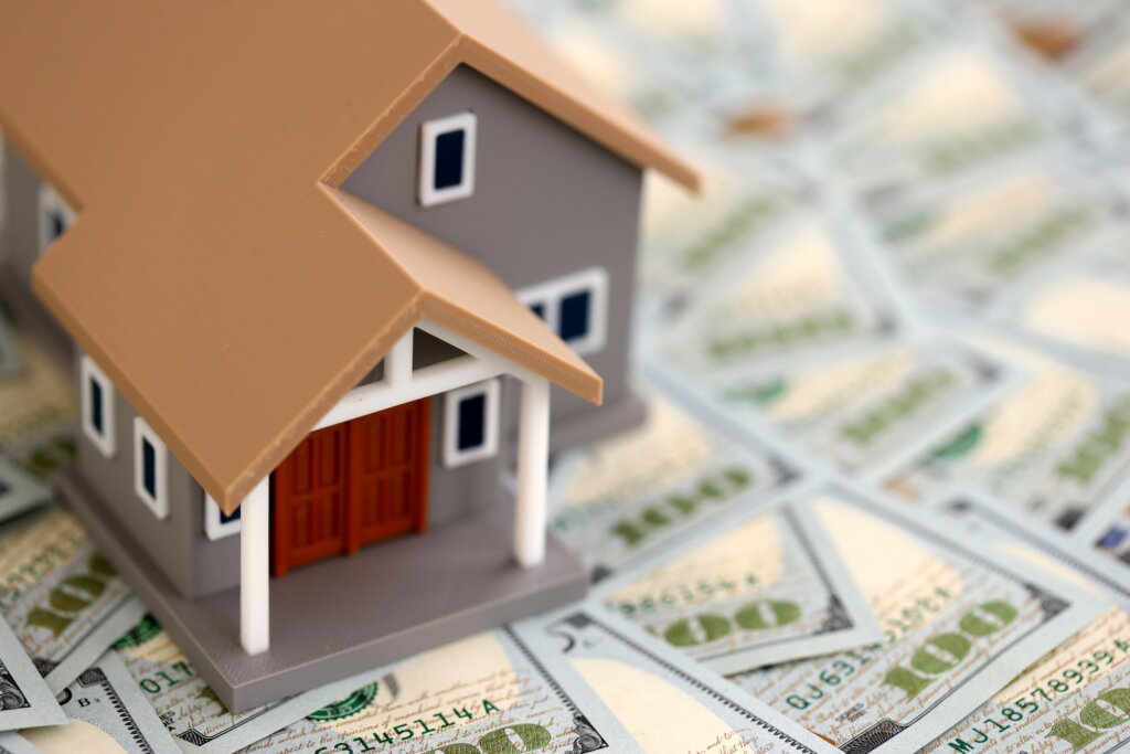 Model house displayed on top of U.S. dollar bills, representing home financing or real estate costs.