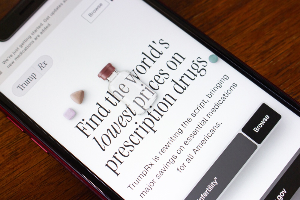 Smartphone displaying the TrumpRx prescription drug pricing website with pills beside the screen.