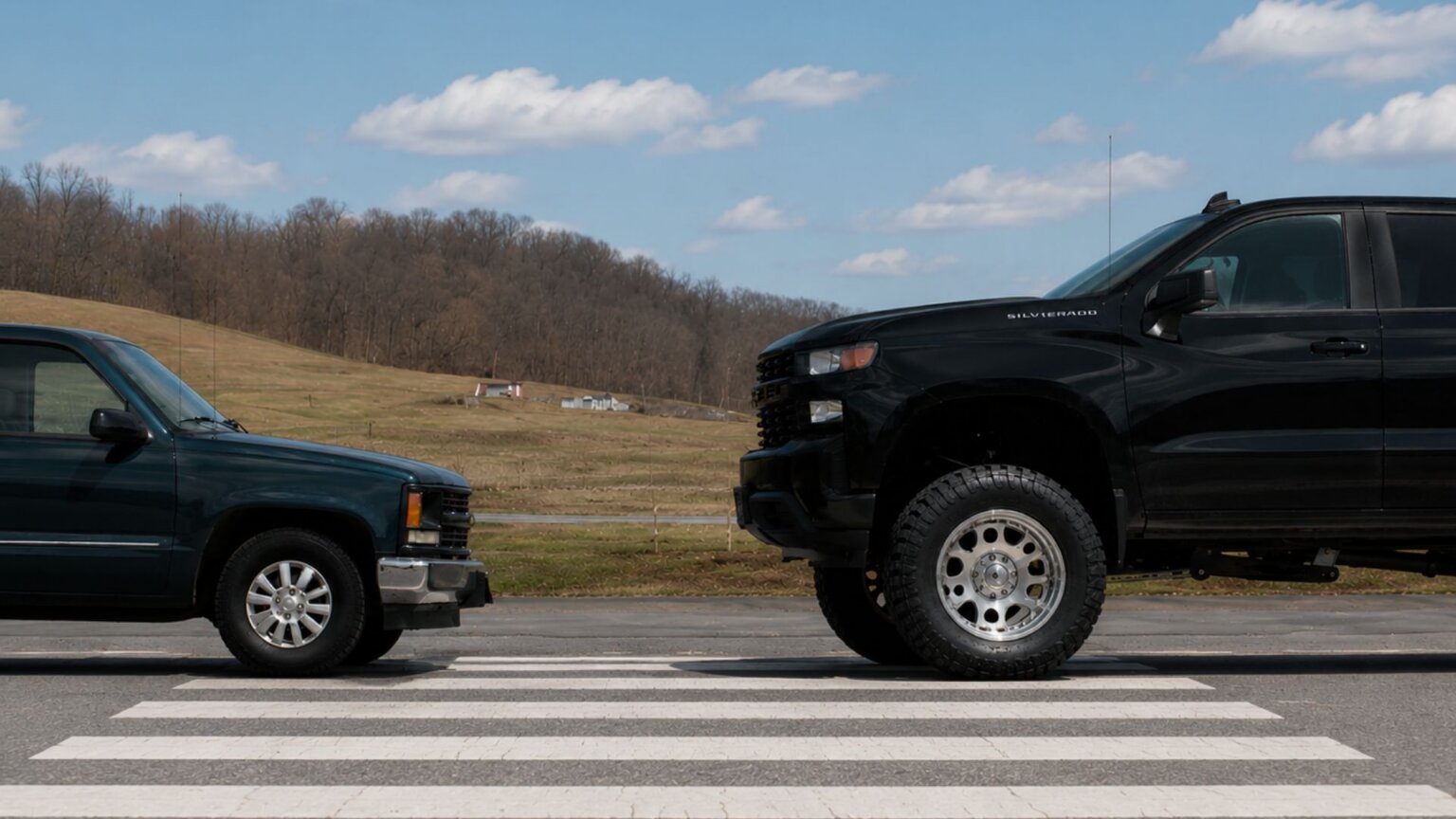 Older pickup truck parked nose to nose with a much taller modern black pickup truck at a painted crosswalk, highlighting the difference in front end height. The side by side comparison illustrates how larger trucks and SUVs have changed in size, providing context for rising pedestrian safety concerns.