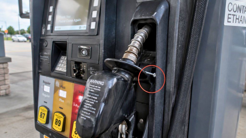 A close-up view of a fuel pump nozzle with a small screw wedged inside the handle, highlighted by a red circle.