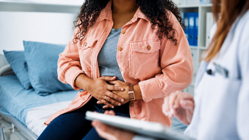 Patient holding their abdomen while speaking with a doctor in an exam room.